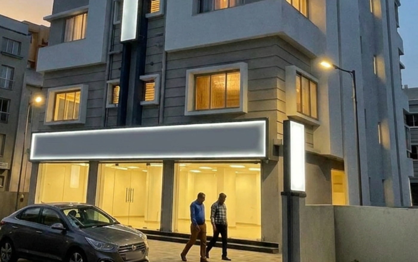 The three glazed retail units at street level, lit at dusk, with the floors above